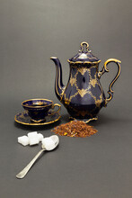 Still Life With A Beautiful Cobalt Blue Colored Vintage Porcelain Tea Set With Golden Floral Pattern, Spoon With Sugar Cubes And Dry Tea Leaves.