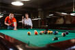 © Dragica - A young caucasian man in a red T-shirt is playing billiards while a girl is standing next to him. Fun time