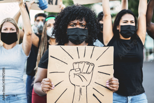 People from different culture and races protest on the street for equal rights with fist banner - Demonstrators wearing face masks during black lives matter fight campaign - Focus on black girl eyes