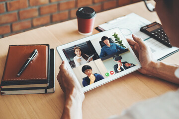 Wall Mural - Asian man working from home use Smart working and video conference online meeting with Asian team using laptop and tablet online in video call for new projects