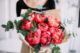 Very nice young woman holding beautiful tender blossoming mono bouquet of fresh coral peony flowers and eucalyptus on the rustic wooden wall background