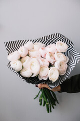 Wall Mural - Very nice young woman holding beautiful blossoming mono bouquet of fresh ranunculus coloney hanoi flowers in tender pink color on the grey background