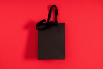 Black friday sale concept. Paper black bag on red background. Shopping concept. Flat lay, top view, copy space