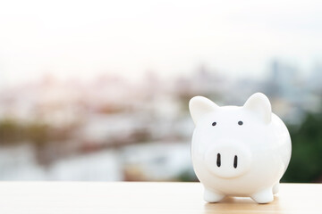 piggy bank white on wooden table and sky, building city background with copy space. Business or finance saving money concept