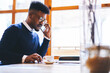 © BullRun - Confident well-dressed afro american entrepreneur having phone conversation with managers controlling work on new startup while waiting for meeting with journalists to give interview about career