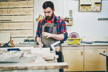 Wall Mural - serious skilled foreman in apron working with instruments and sharp tool repair wooden details, prof