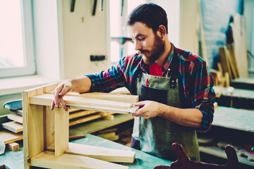 Wall Mural - handsome bearded man working with wooden construction in own small-sized furniture company, caucasia
