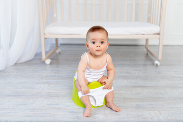 small baby girl 8 months old sitting on a potty, baby toilet, place for text