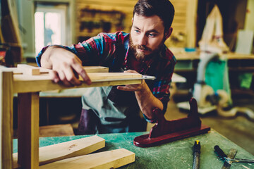 Wall Mural - skilled bearded caucasian male master working with wood making stool in workshop owning manufacture 