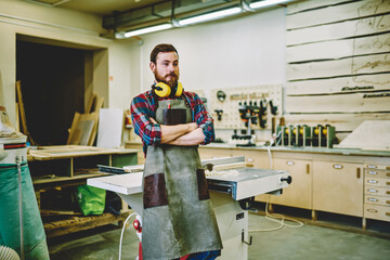 Wall Mural - successful self-employed woodman in work apron standing in own manufacturing fabric with crossed han