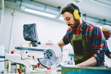 Wall Mural - caucasian man in headphones using circular for work with wood and timber in workshop with safety, sk