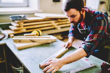 Wall Mural - serious bearded male maker checking measures of wooden bricks with ruler planning construction and e