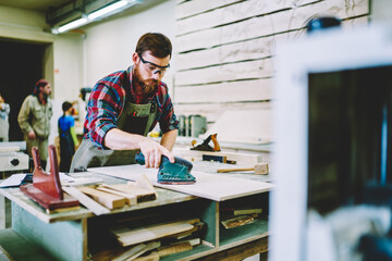 Wall Mural - serious bearded male in eyewear for protection working with electric instrument for polish wooden pl