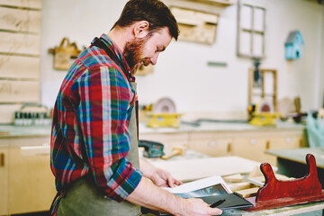 Wall Mural - smiling male owner of crafts workshop checking planning and organizing working day in notebook, posi