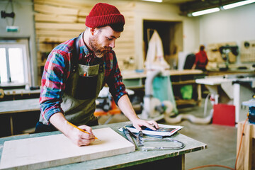 Wall Mural - professional male student of crafts courses using instructions for making detail from wood in worksh