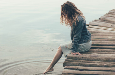 
The girl is sitting on a post near the river, the girl is wetting her feet in the river and smiling