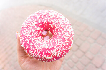 Pink doughnut in woman's hand with copy space. Dessert festive. donut with a pink chocolate frosting. Breakfast and hen-party concept. Snack and junk food habit. Sweet gift for daughter, girl, mother