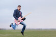 Guitar hipster guy jumping and playing funky rock music outdoors