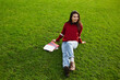 © BullRun - Attractive asian student girl relaxing after class sitting with pile of books on beautiful green grass copy space area for text