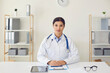 © Studio Romantic - Female hispanic doctor looking at the camera listens to a patient uses a webcam conference while sitting at a table in the office of a medical clinic.