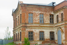 The Abandoned House Has 2 Floors. Large Windows With Bars On A Brick Old House. The Estate Of The Late 18th Century. Residential Building Of The Last Century Is Made Of Red Brick. Antique Brickwork