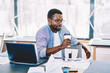 © BullRun - Serious african american guy holding cardboard cup thinking about job on work break, pensive dark skinned male freelancer sitting at desktop with coffee thoughtfully looking away in coworking space.