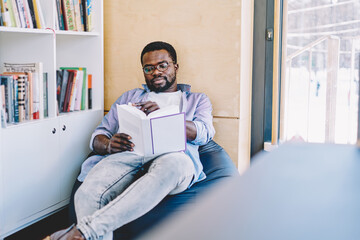 Man reading book on bean bag near window