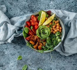 Wall Mural - Buddha bowl salad with baked sweet potatoes, chickpeas, broccoli, tomatoes, greens, avocado, pea sprouts on light blue background with napkin. Healthy vegan food, clean eating, dieting, top view