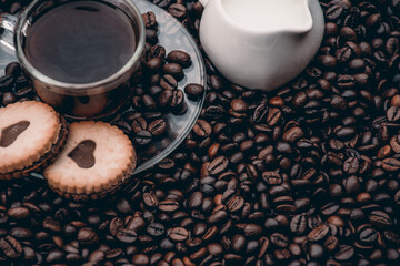  a cup of black coffee, two cookies and milk beside it. black coffee beans in the background