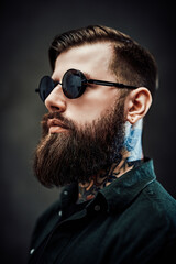 Wall Mural - Profile of a young bearded barber with tattoo on his neck in a dark studio