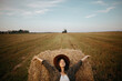 © sonyachny - Stylish girl relaxing on hay bale in summer field in sunset. Portrait of young sensual woman in resting at haystack, atmospheric tranquil moment. Countryside slow life