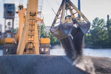 Bulk-handling crane unloading sand, road metal and gravel from cargo vessel ship, heavy vehicle and portal crane loader working with bulk materials in dock terminal