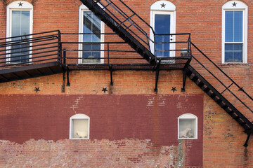 Wall Mural - arched white windows behind back alley fire escape stairs at an old faded brick building