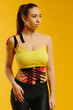 © dsheremeta - Young caucasian girl with kinesiology tape on her belly and leg, on yellow background. Sport and rehabilitation, kinesiotherapy treatment.