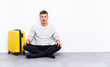 © luismolinero - Young handsome man sitting on the floor with a suitcase with surprise facial expression