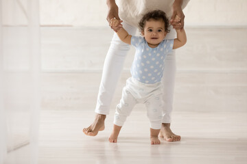 Wall Mural - caring barefoot african american mother teaching cute toddler daughter to walk, loving mum holding c
