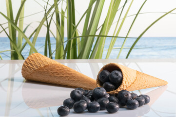 Two tempting ice cream cones with a bunch of delicious looking blueberries on a glass table