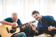© chokniti - happy adult son and senior father playing guitar on sofa at home relaxing and having happy time with family