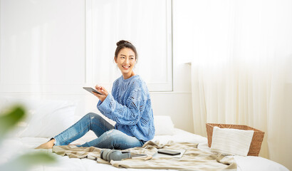 Asian woman with smile use tablet smartphone in blue winter sweater work home, Portrait young beauty asia girl relax in bedroom. Technology people connection digital online market banner