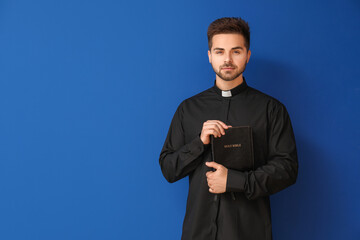 Wall Mural - Young priest with Bible on color background