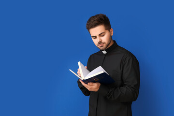 Wall Mural - Young priest reading Bible on color background