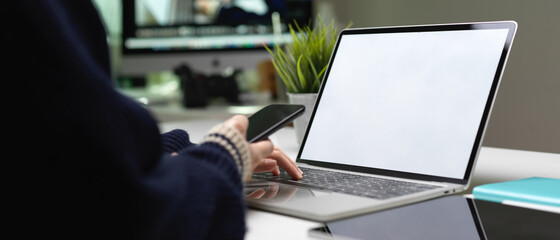Female worker right hand holding smartphone and left hand typing on laptop keyboard