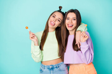 Poster - Photo of two funny crazy lady hold lollipop chupa chups hands sweets addicted stick tongue out mouth wear cropped pullovers naked belly skirts isolated pastel teal color background