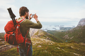 Man travel blogger taking photo by smartphone hiking with backpack in mountains influencer lifestyle adventure summer tour outdoor in Norway