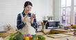 © PRPicturesProduction - young happy asian korean woman in apron looking at recipe in smart phone in kitchen counter. girl cooking at home preparing healthy vegetable salad. beautiful smiling female using cellphone by window