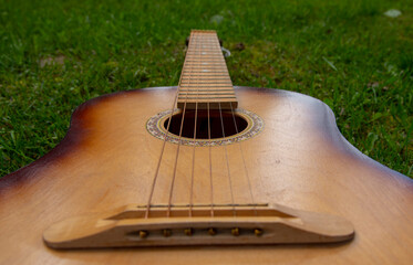 An acoustic wooden guitar is lying on a green lawn.