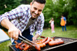 © NDABCREATIVITY - Handsome male preparing barbecue, grill outdoors for friends