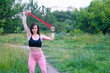 © reddish - Woman exercising with elastic band outdoors in the park. Young muscle girl.