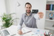 © ViDi Studio - Cheerful young bearded business man in gray shirt sit at desk work on laptop pc computer in light office on white wall background. Achievement business career concept. Hold in hand credit bank card.
