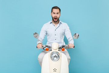 Wall Mural - Shocked worried young bearded man guy in casual light shirt driving moped isolated on pastel blue background studio. Driving motorbike transportation concept. Mock up copy space. Keeping mouth open.